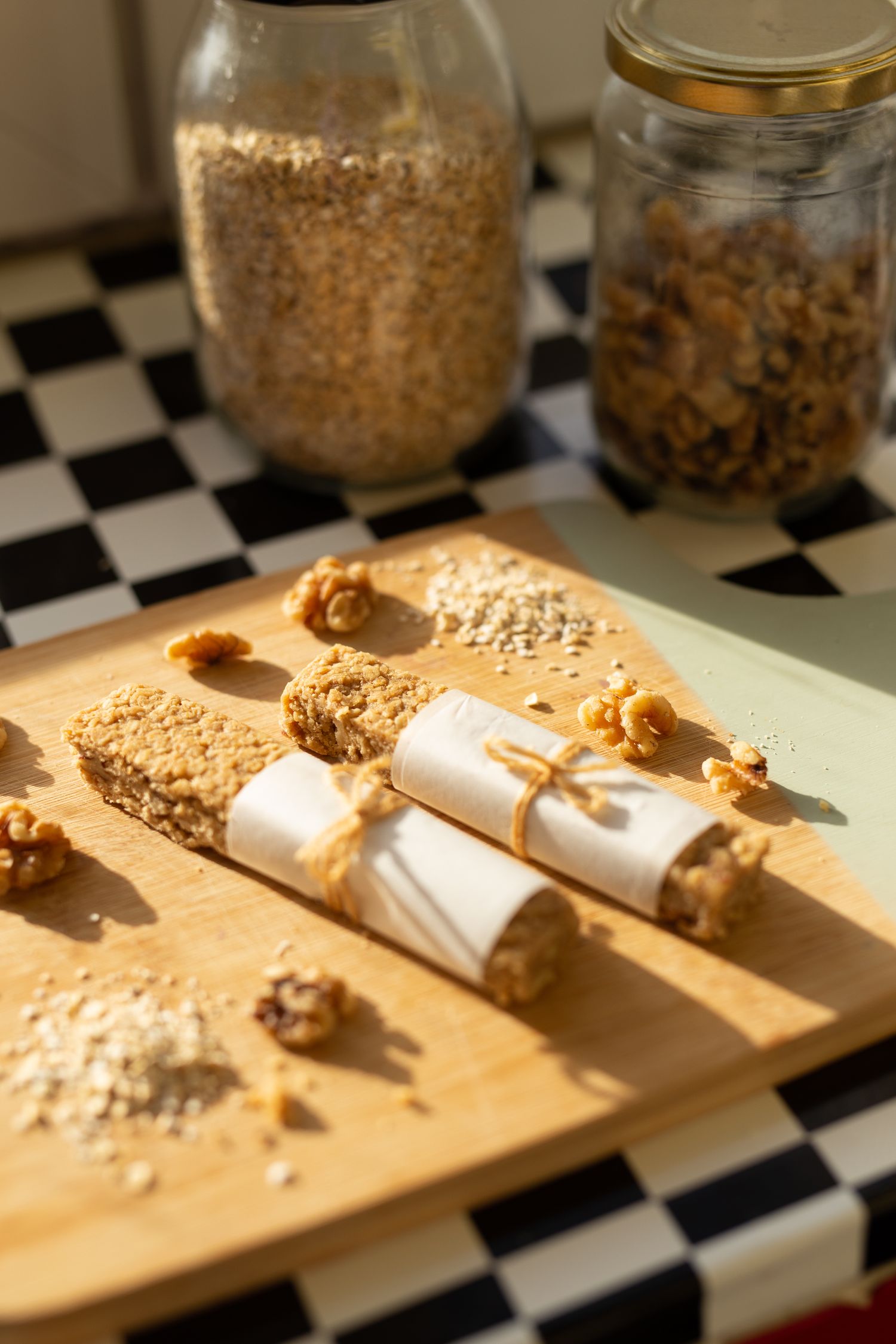 Homemade granola bars and jars of oats on a checkered surface in warm lighting.