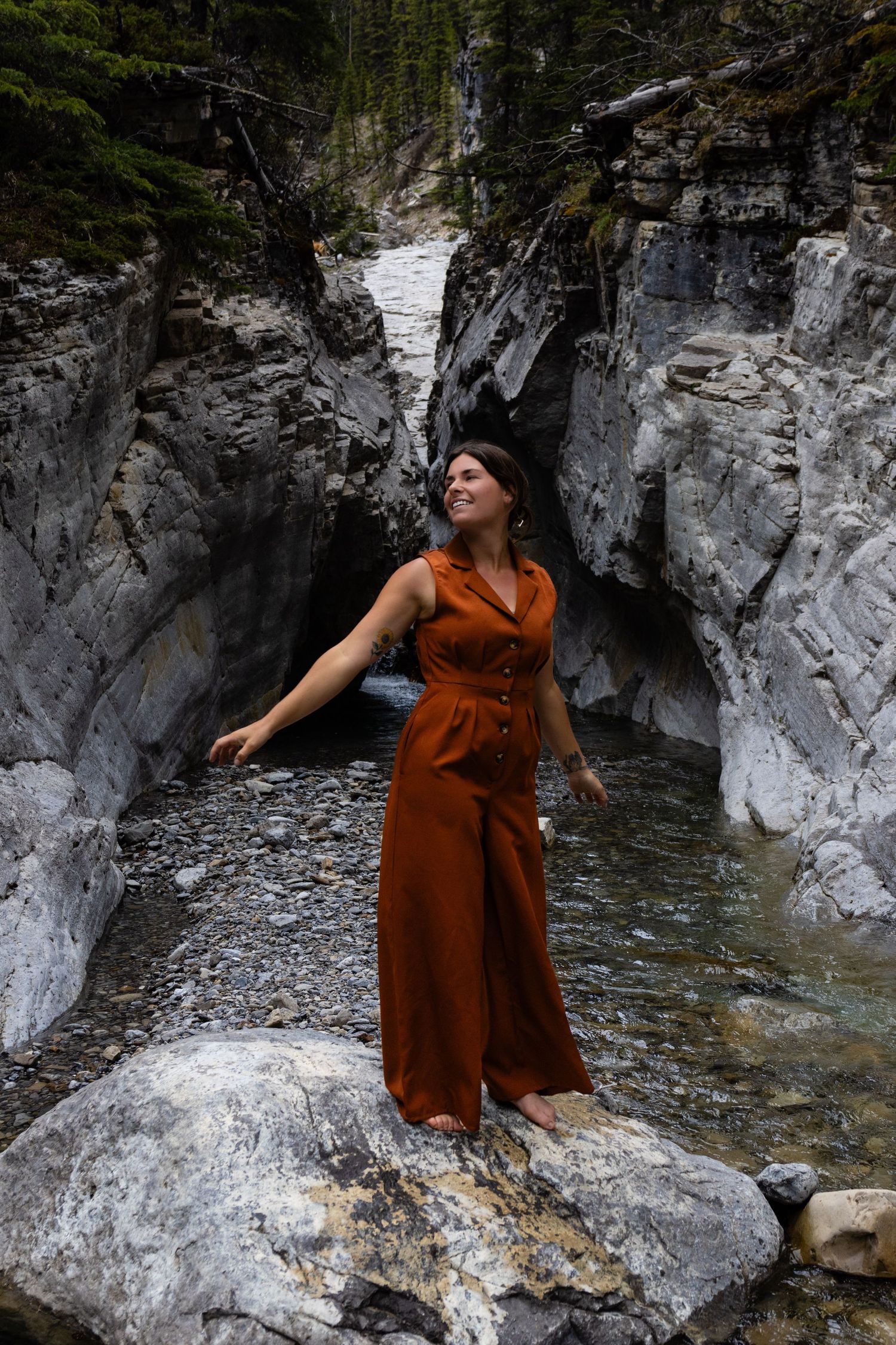 A dramatic pose on rocky terrain with a flowing rust-colored jumpsuit near a mountain stream.