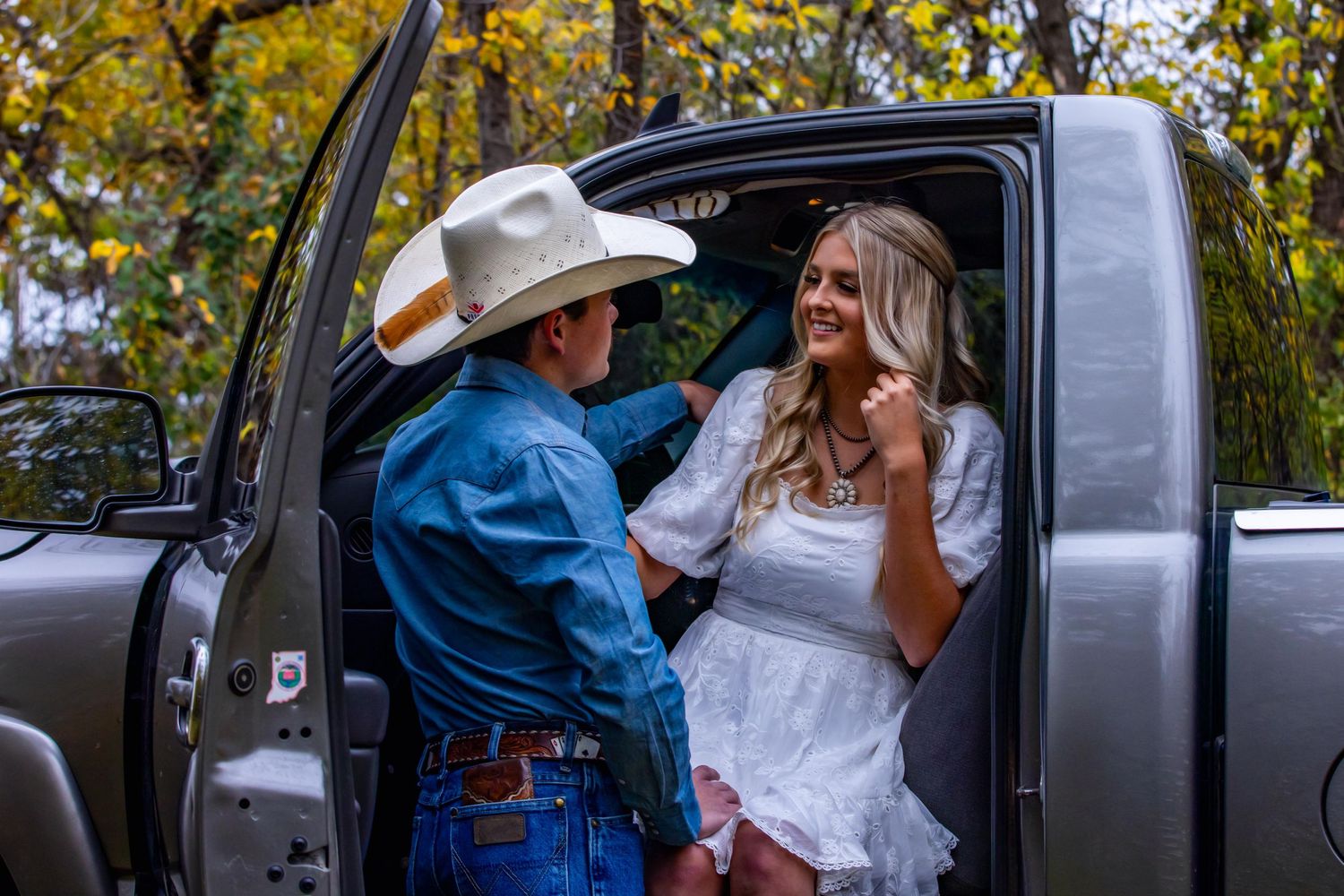 A couple sharing an intimate moment by their pickup truck with autumn trees in the background.