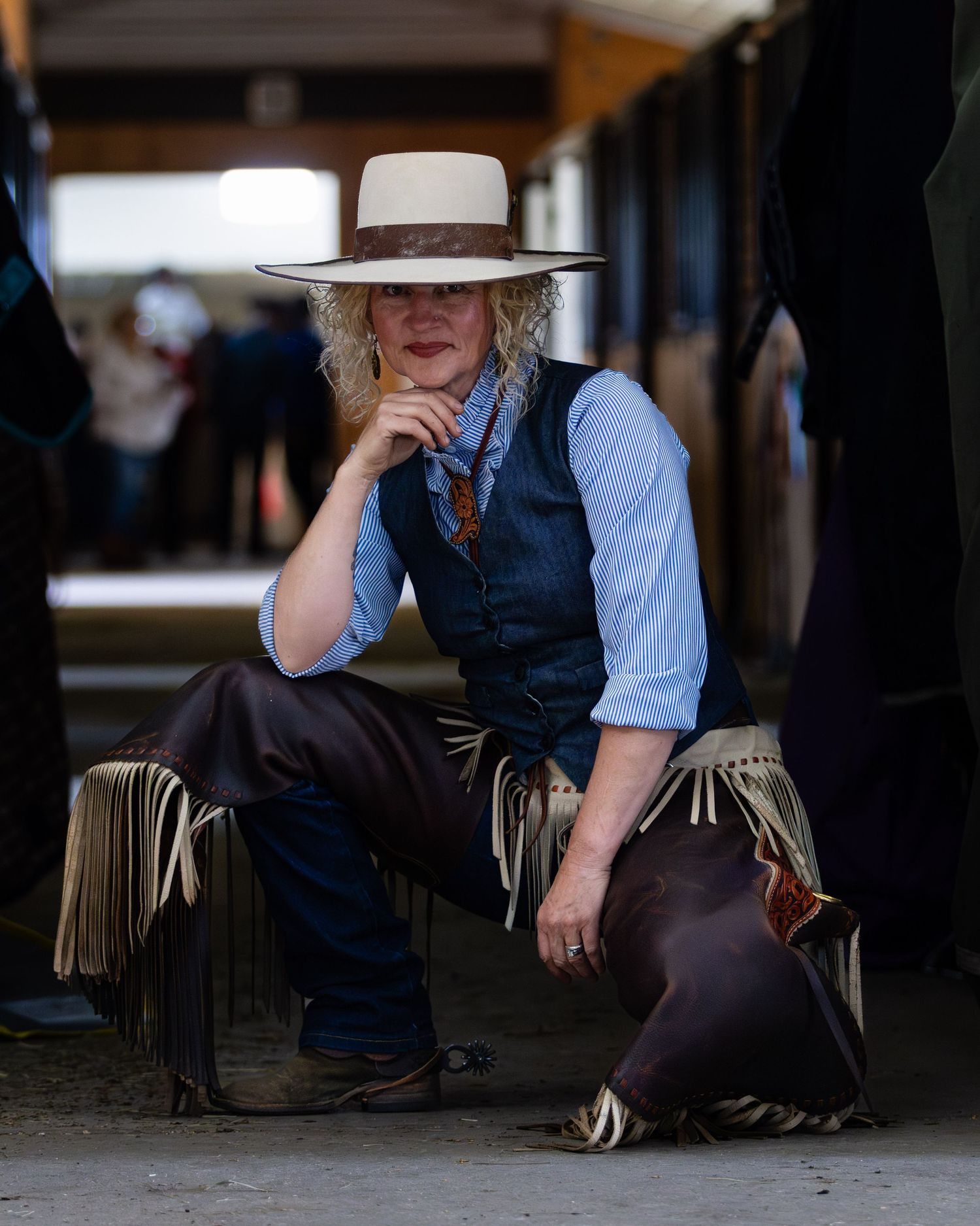 Person in western attire and hat seated in contemplative pose indoors.