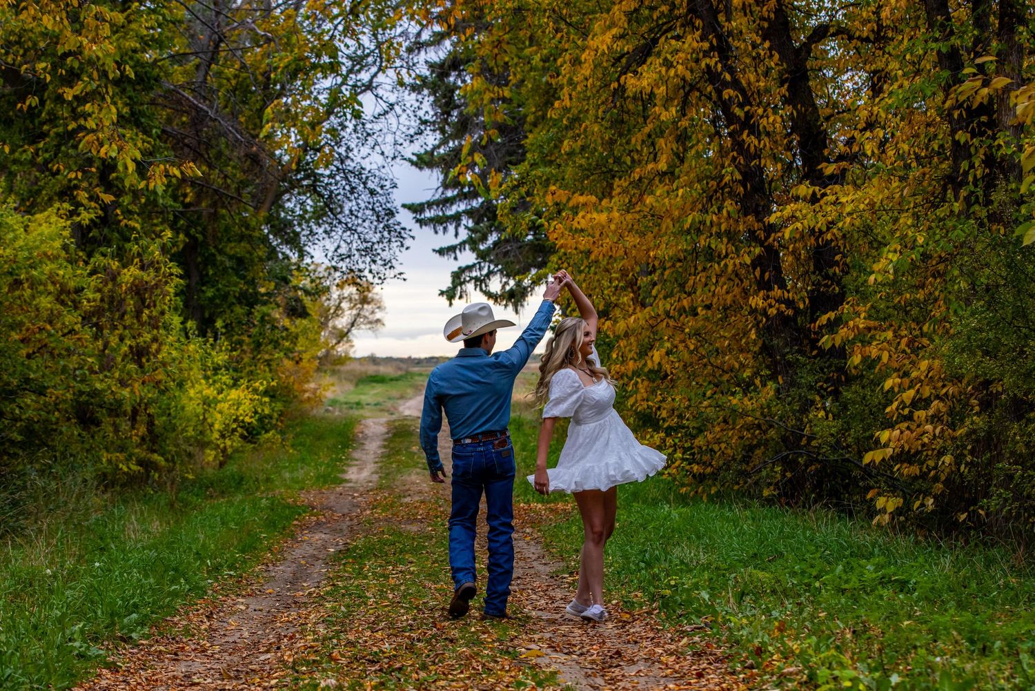A couple dancing together on a rural path surrounded by autumn trees.