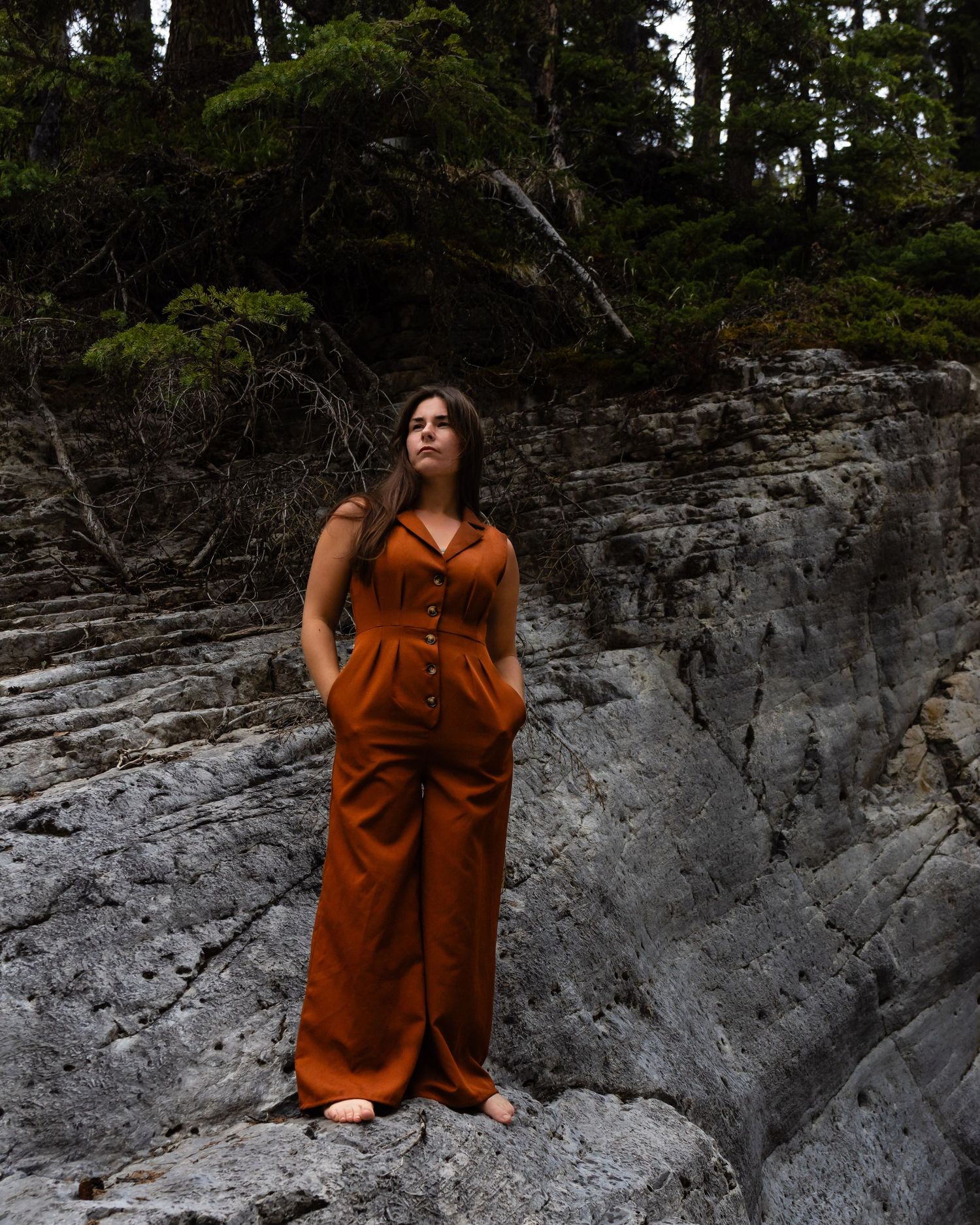 A stylish rust jumpsuit contrasts against dramatic gray rock formations in nature.