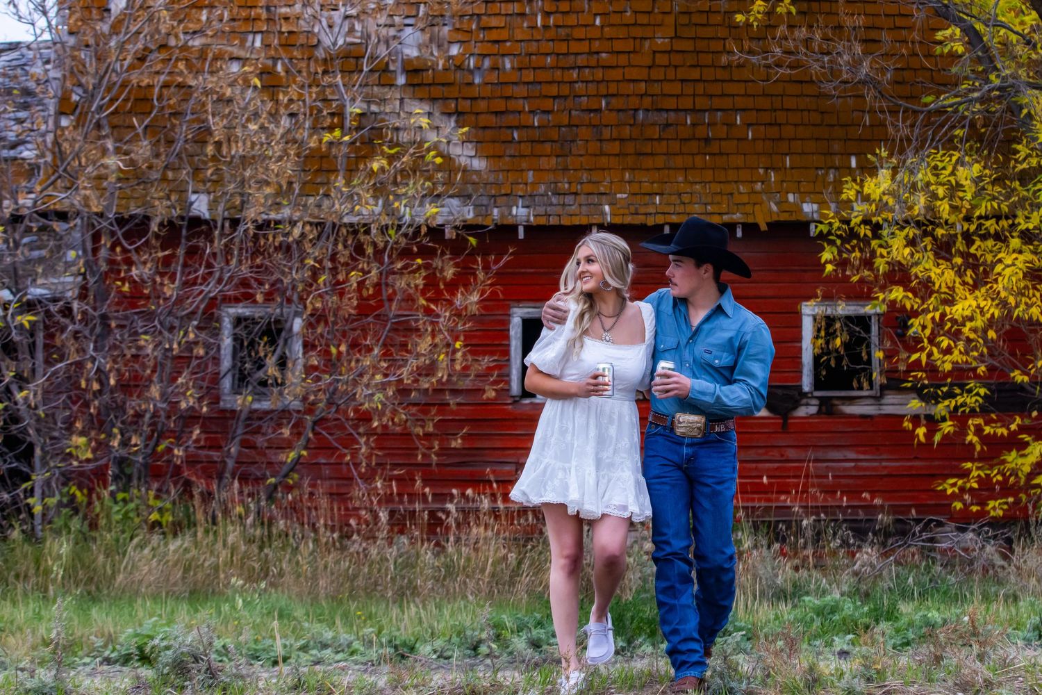 A couple posing together against a rustic red barn wall in autumn.