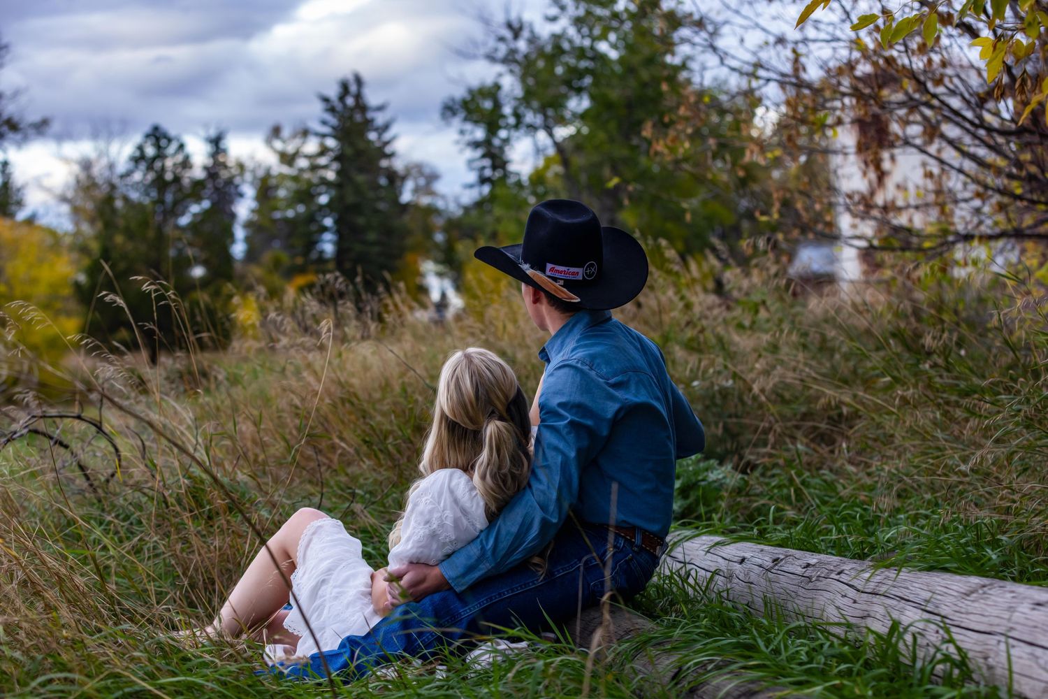 A couple relaxing together on a log amid tall grass and autumn foliage.
