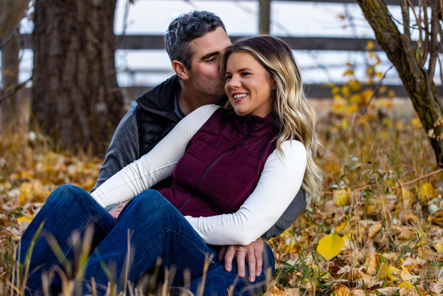 A loving couple embraces while sitting in autumn leaves wearing cozy sweaters on a fall day.