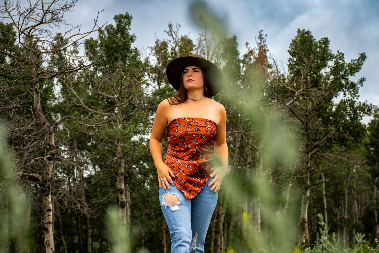 A western style portrait with a brown hat and red top among green foliage.