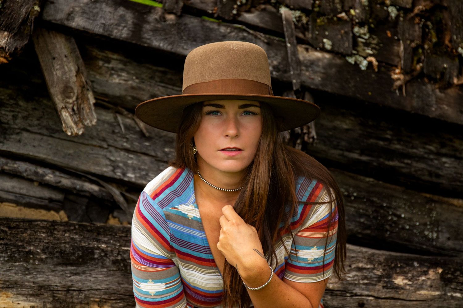 A rustic portrait against weathered wood wearing a brown hat and striped dress