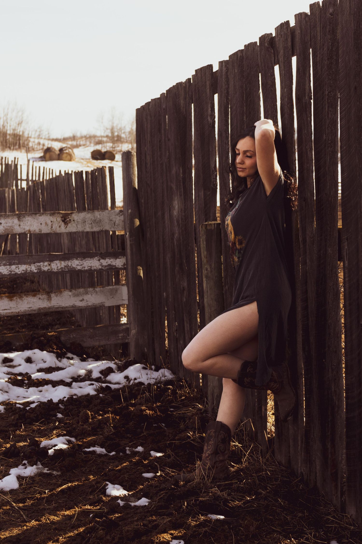 A artistic winter portrait against a rustic wooden fence with patches of snow on the ground.