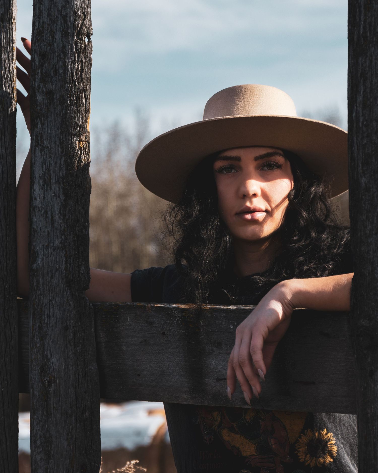 A rustic portrait through wooden fence posts featuring a wide-brimmed hat and natural lighting.