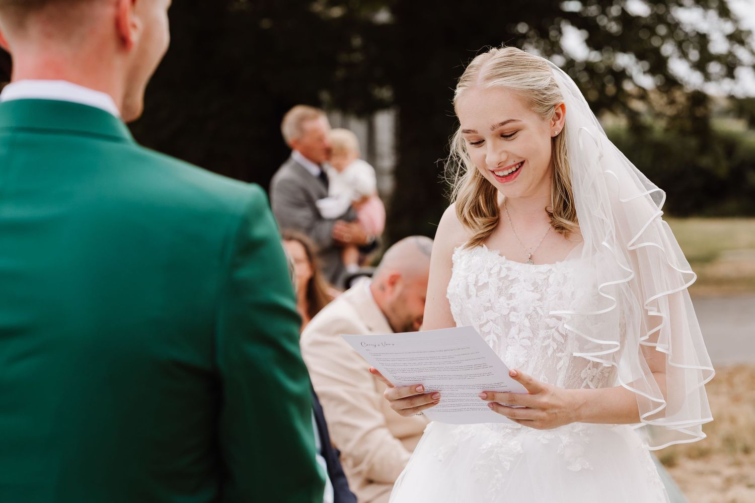 Smiling bride in white gown and veil reading wedding vows outdoors at Moor Farm, Weymouth, Dorset