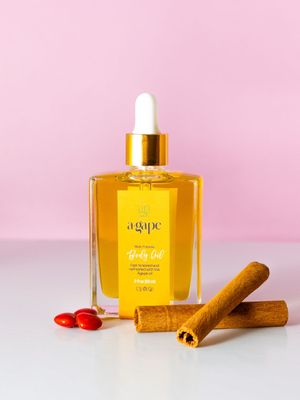 Amber essential oil bottle with cinnamon sticks and red berries against a pink background.
