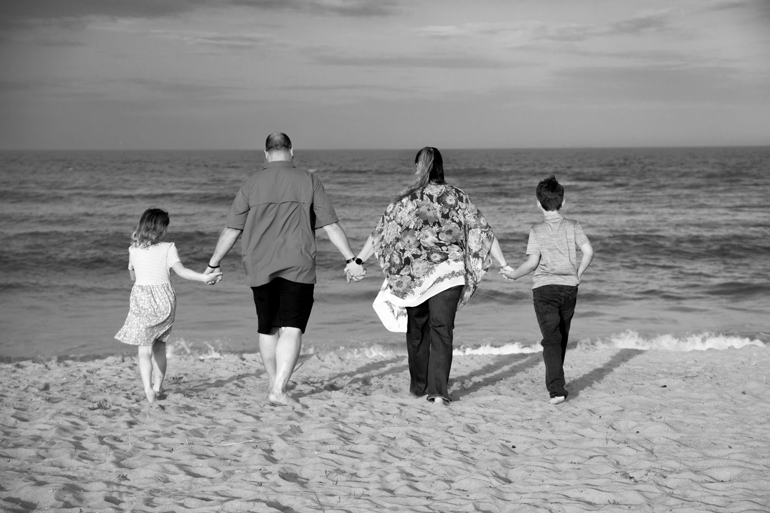 A group of people walking together hand in hand on a beach towards the ocean in black and white.