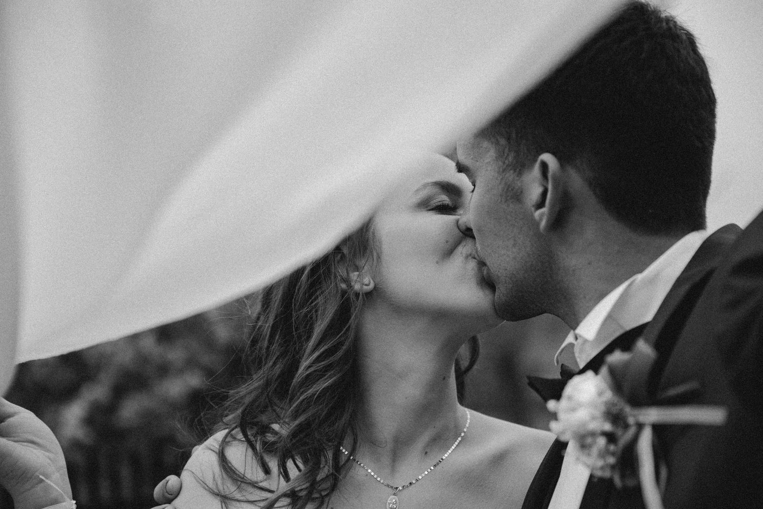 Romantic moment captured under flowing white veil during wedding celebration.