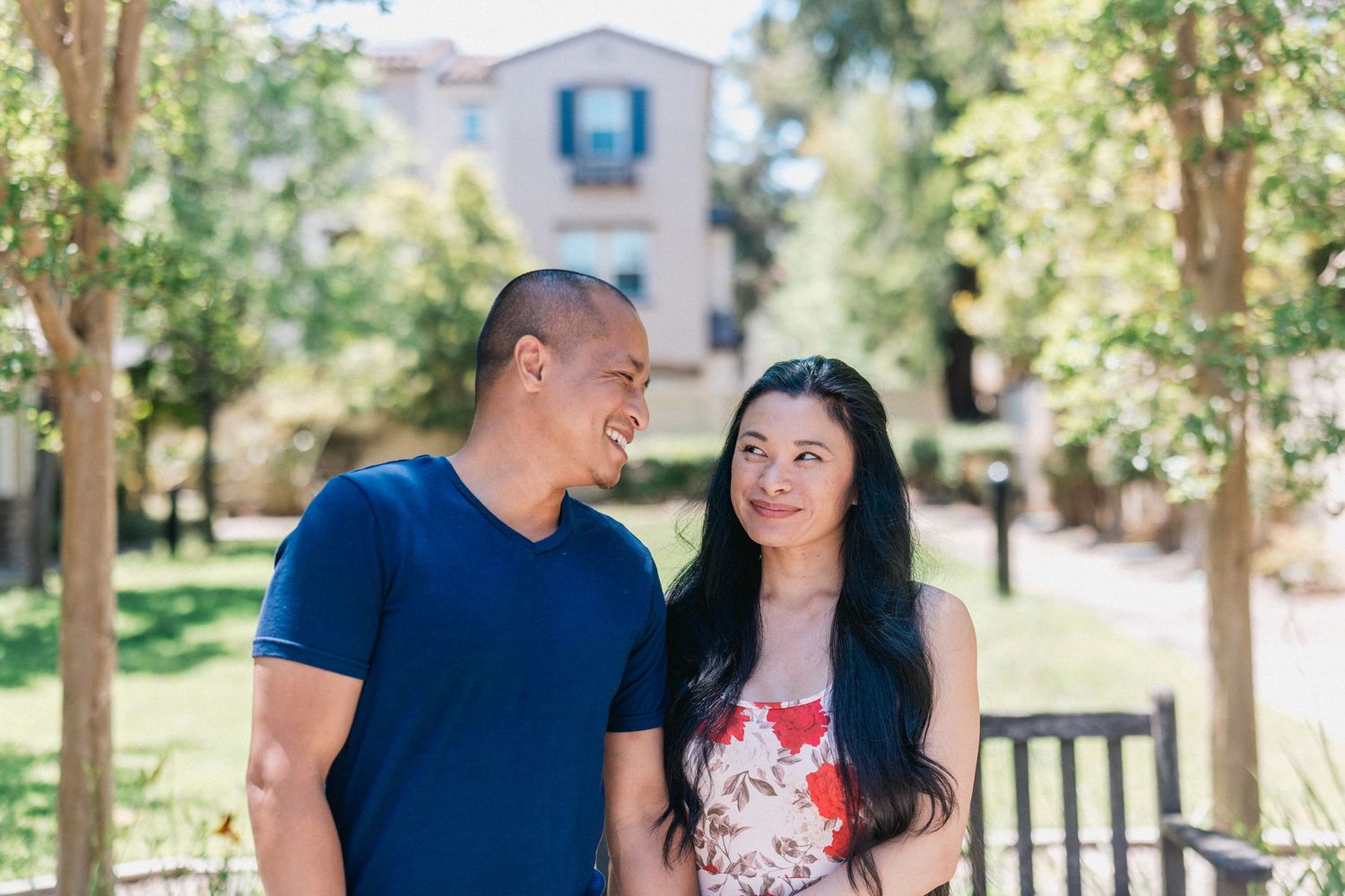 Couple sharing a tender moment while standing on tree-lined path near building.