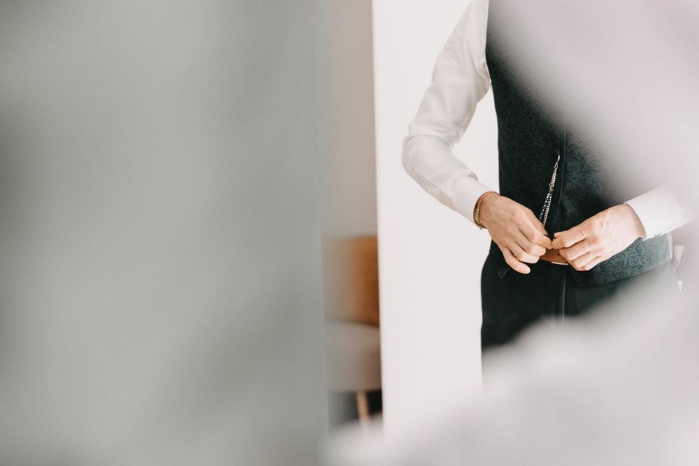 Cropped view of hands adjusting formal attire against white wall.