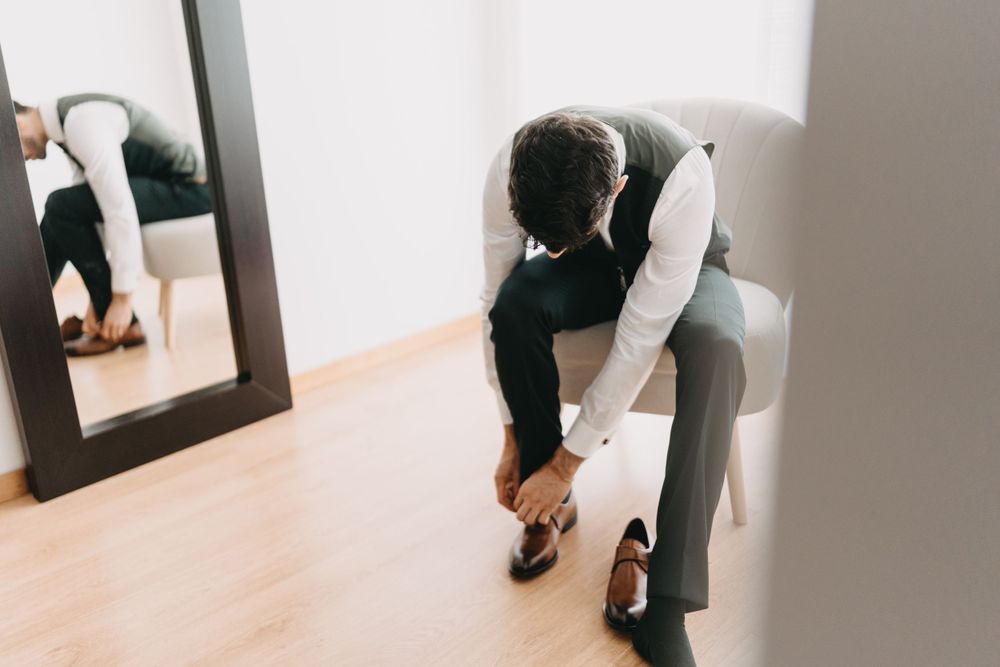 Person in formal attire bending down to adjust shoes in front of mirror.