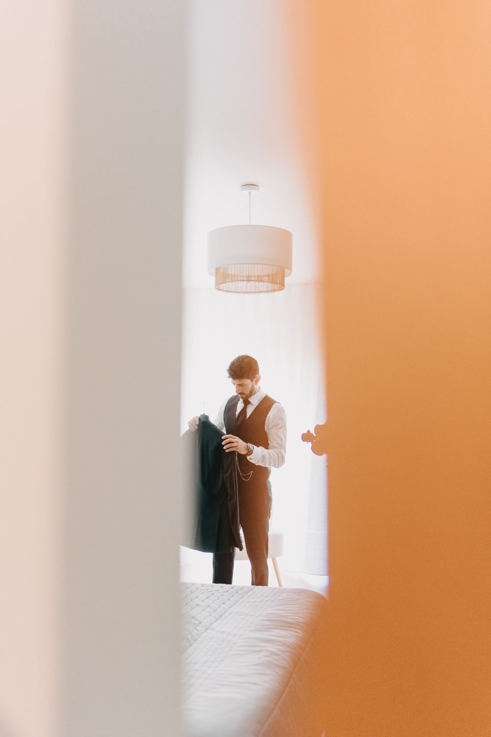 Figure in formal attire viewed through doorway reading document in minimalist white interior.