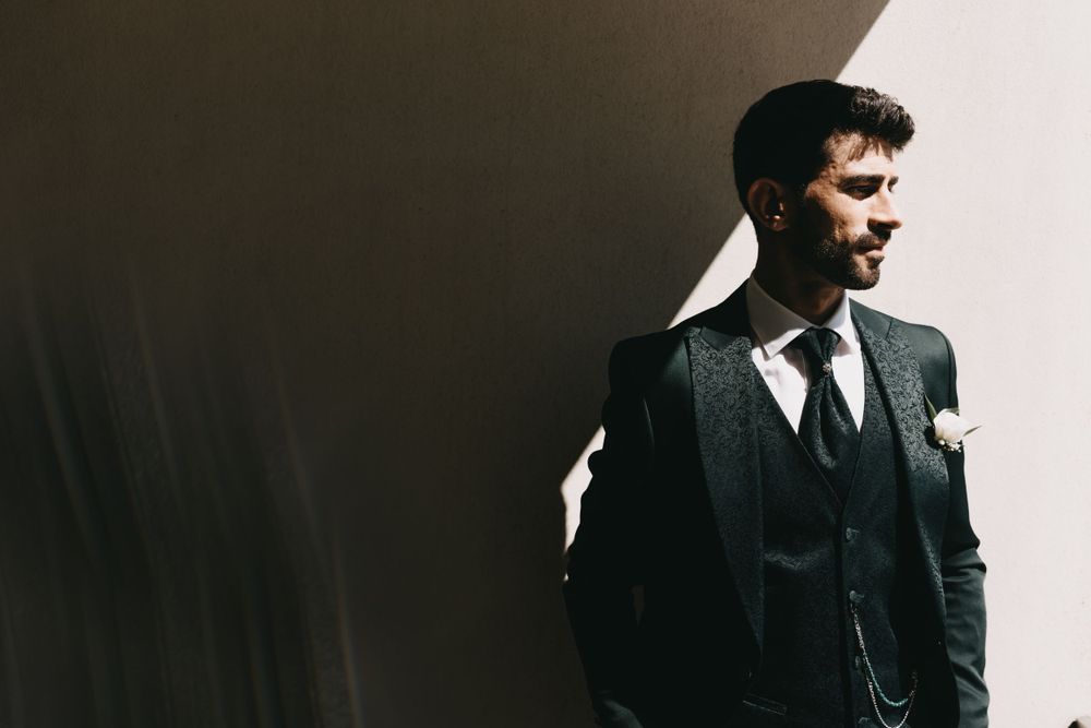Dramatic high contrast portrait of groom in three-piece suit against dark background.