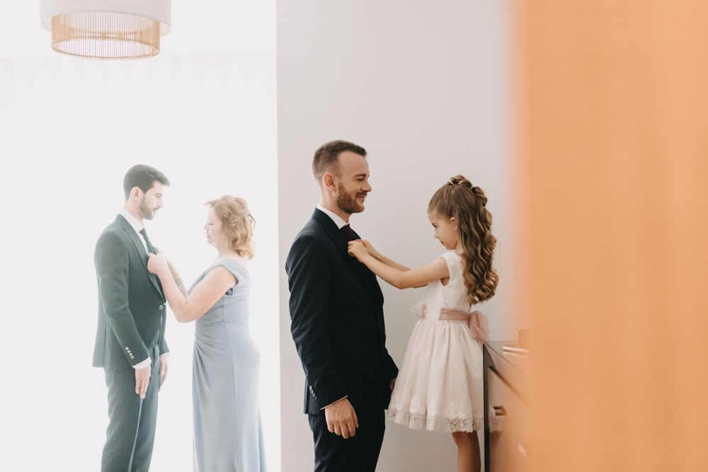 Wedding party members share intimate moments in a bright white room with peach accents.