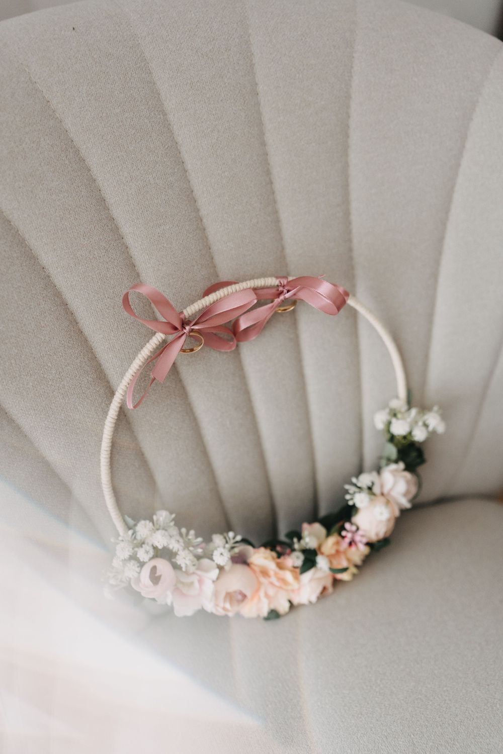 Delicate floral hoop with pink roses and white flowers adorned with satin ribbon against a textured background.