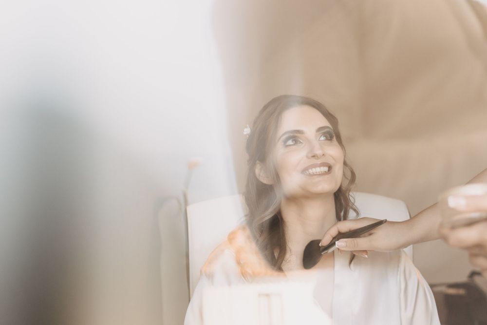 A dreamy bridal preparation moment captured through soft focus as makeup is being applied on a smiling person.