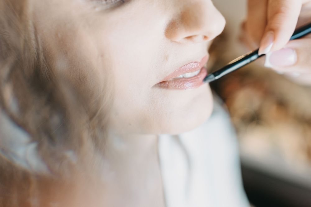 Close-up of makeup brush applying lipstick during bridal preparation.