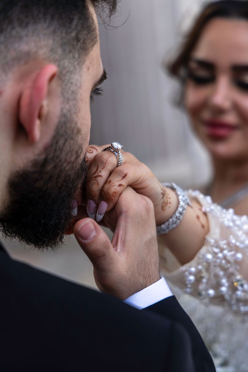 A tender moment at a wedding where a groom kisses his bride's ring-adorned hand against a soft blurred background.