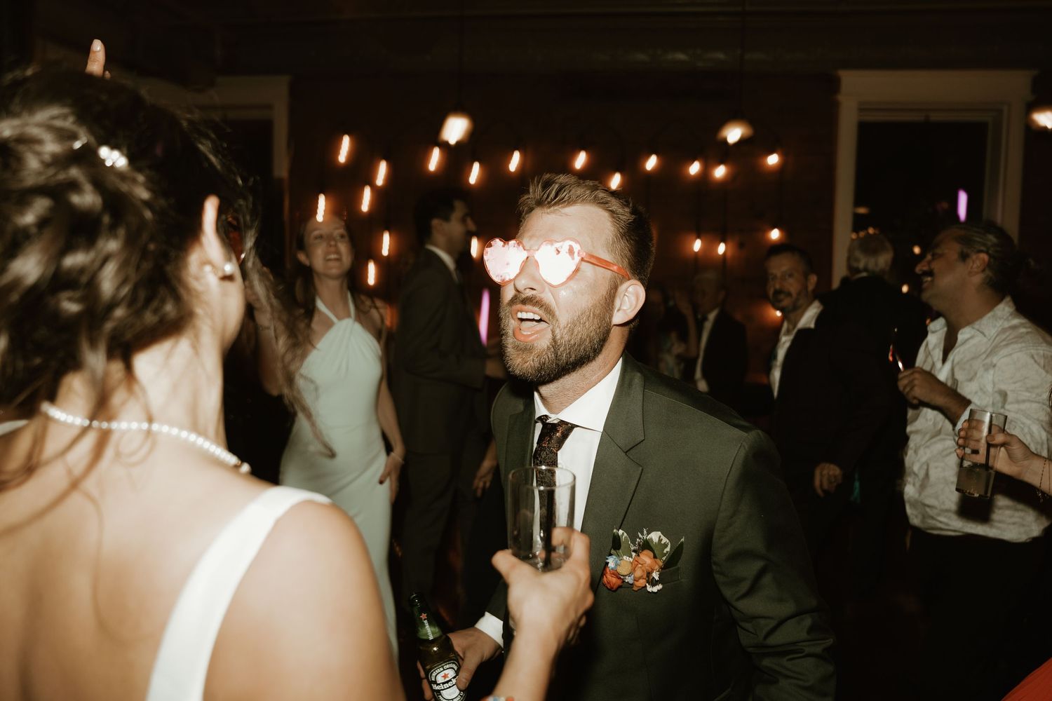 Guests are enjoying a wedding reception in a dimly lit venue with festive dancing and mingling.