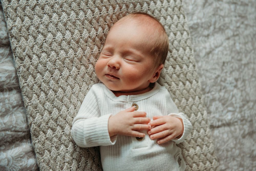 A peaceful sleeping baby wearing a white sweater lies on a textured gray blanket.