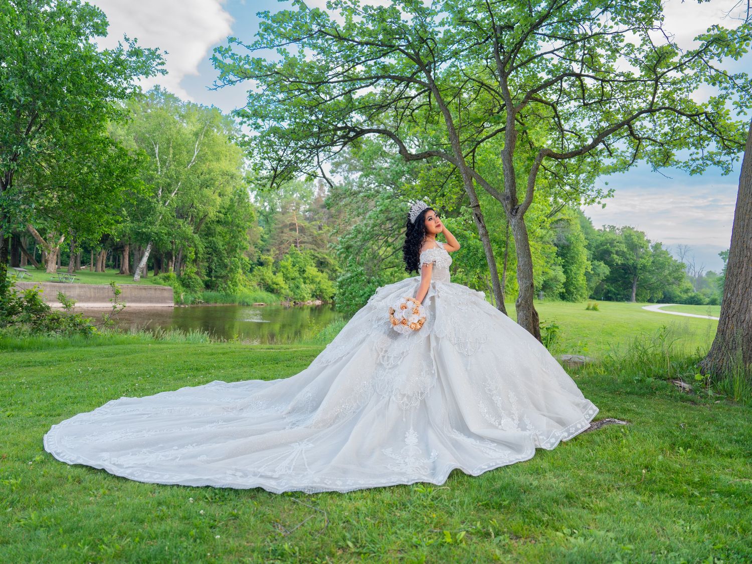 Dramatic white Quinceañera gown with cathedral train displayed across green lawn.