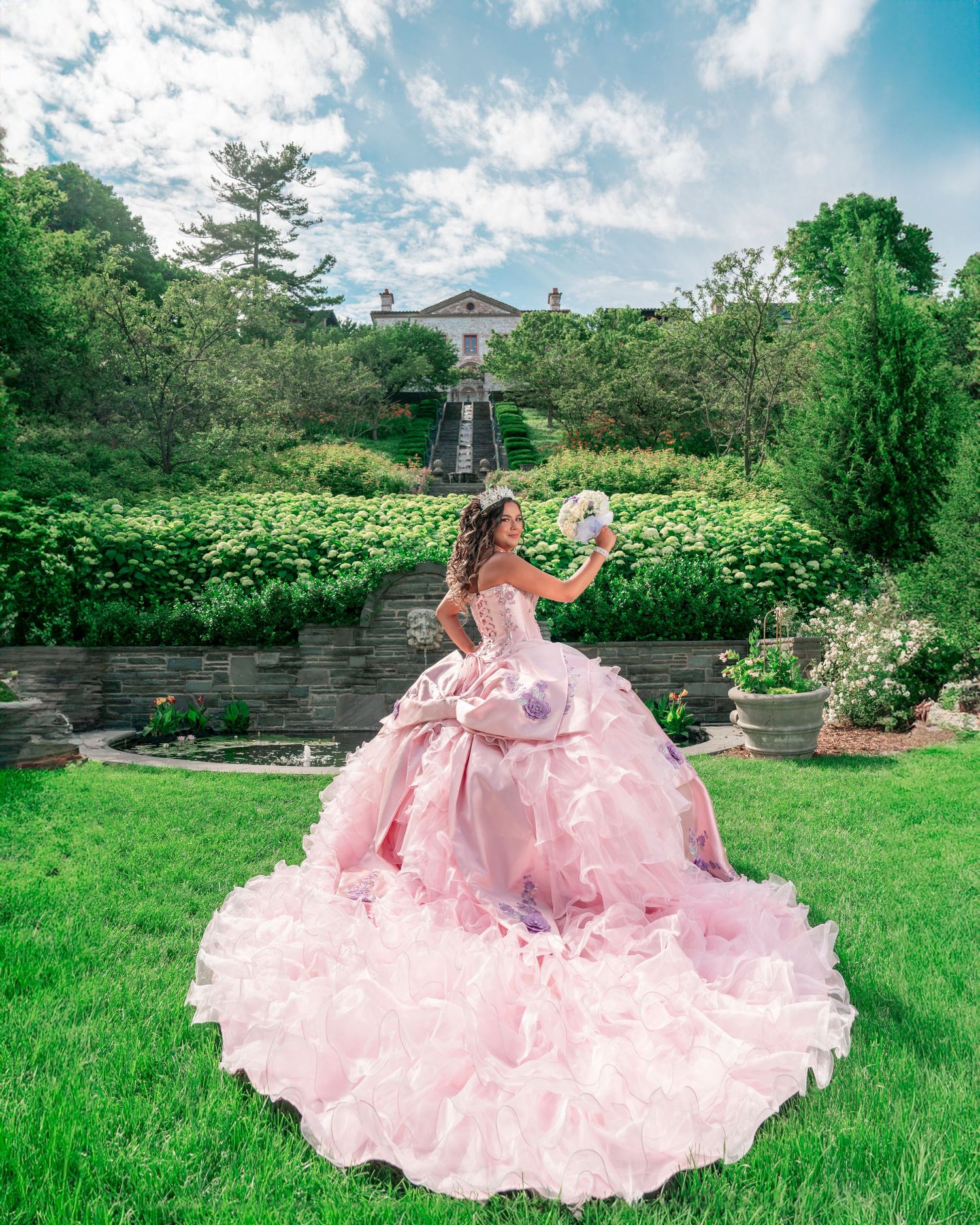 Pink floral quinceañera dress flowing across green garden lawn in elegant outdoor photoshoot. Quineañera photos at Milwaukee Museum.