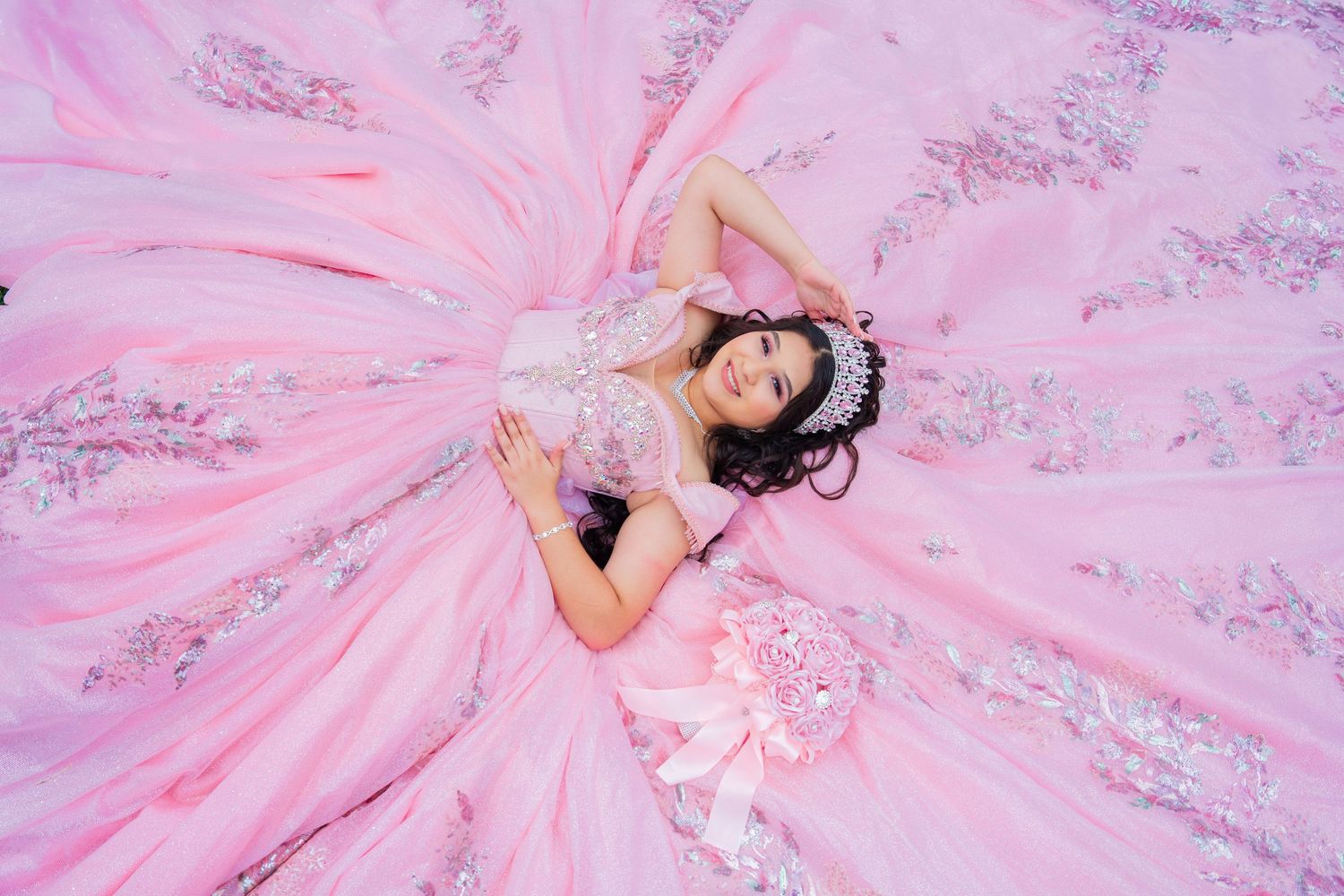 Flowing pink princess gown with detailed embroidery and a dramatic train spread out on garden path. Quinceañera