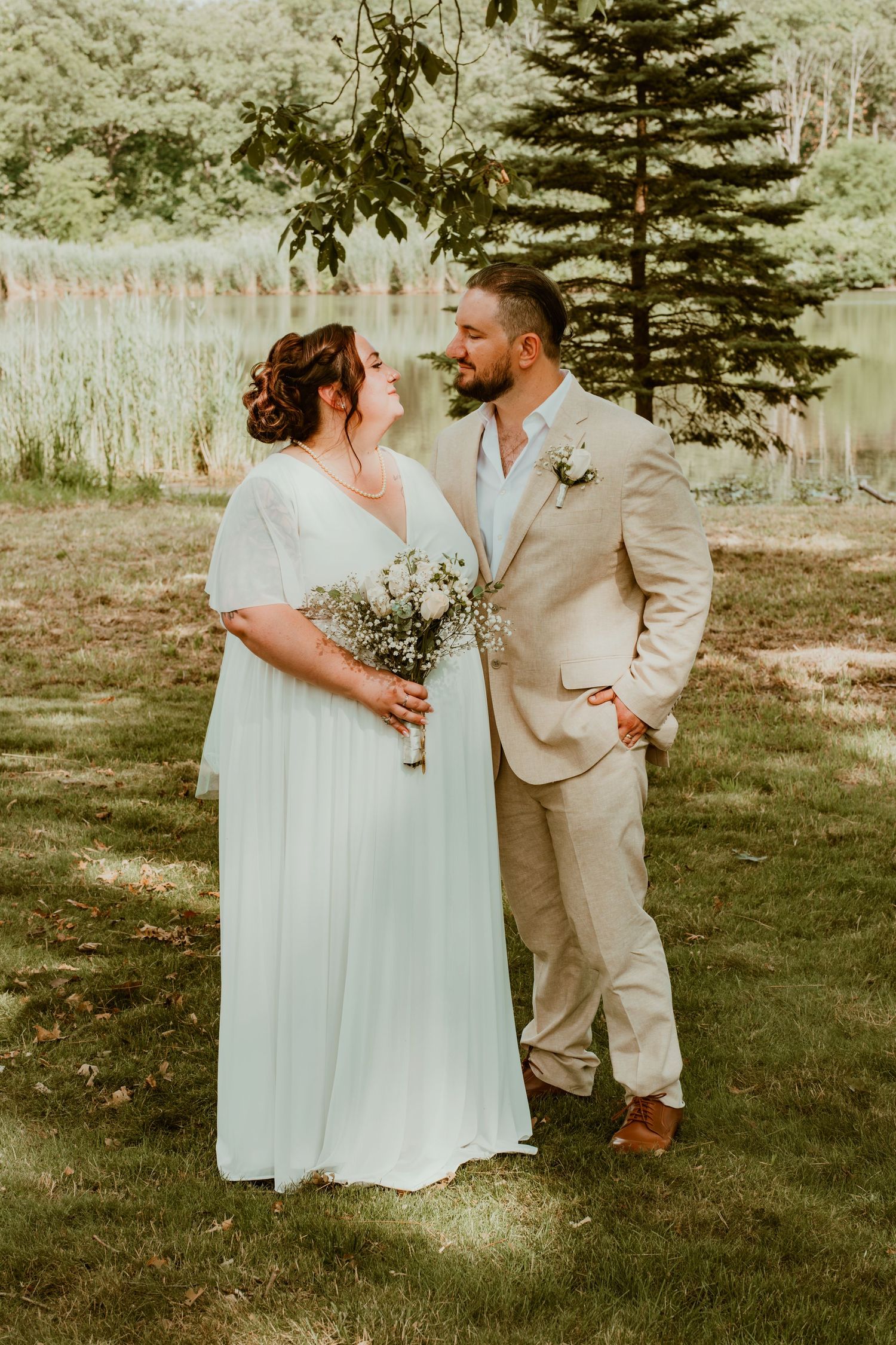 Bride and groom share a romantic moment outdoors with pine trees and lake in background.