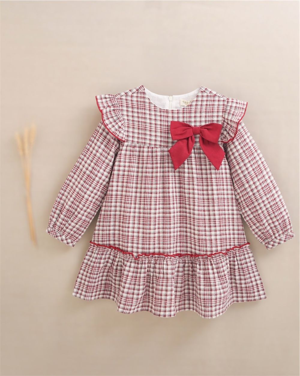 Red plaid long-sleeve girls dress with ruffled hem and large red bow accent on the chest.