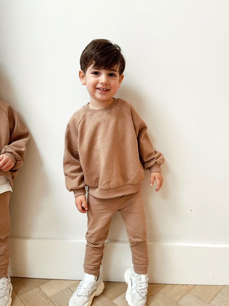 A small child poses in a matching tan sweatsuit and white sneakers against a white wall in multiple photos.