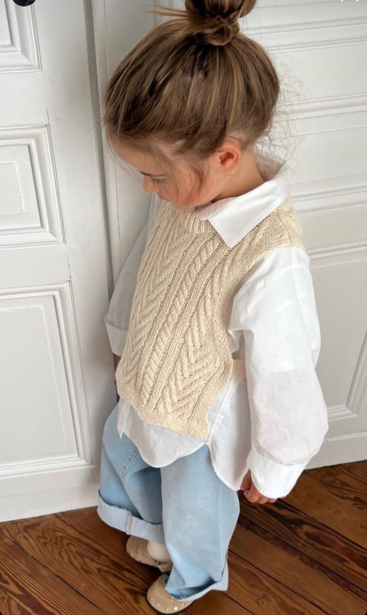 Candid view from behind of person wearing cream knit vest and white blouse against white wall.