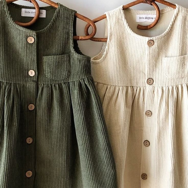 Collection of sage green and cream colored ribbed baby rompers with button details hanging on wooden hangers.