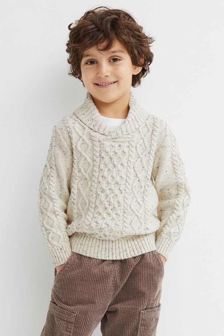 Child wearing a cozy cream cable knit sweater and brown corduroy pants against a white background.