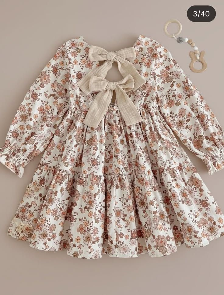 White floral long sleeve tiered toddler dress with large bow back detail in pink and brown tones.