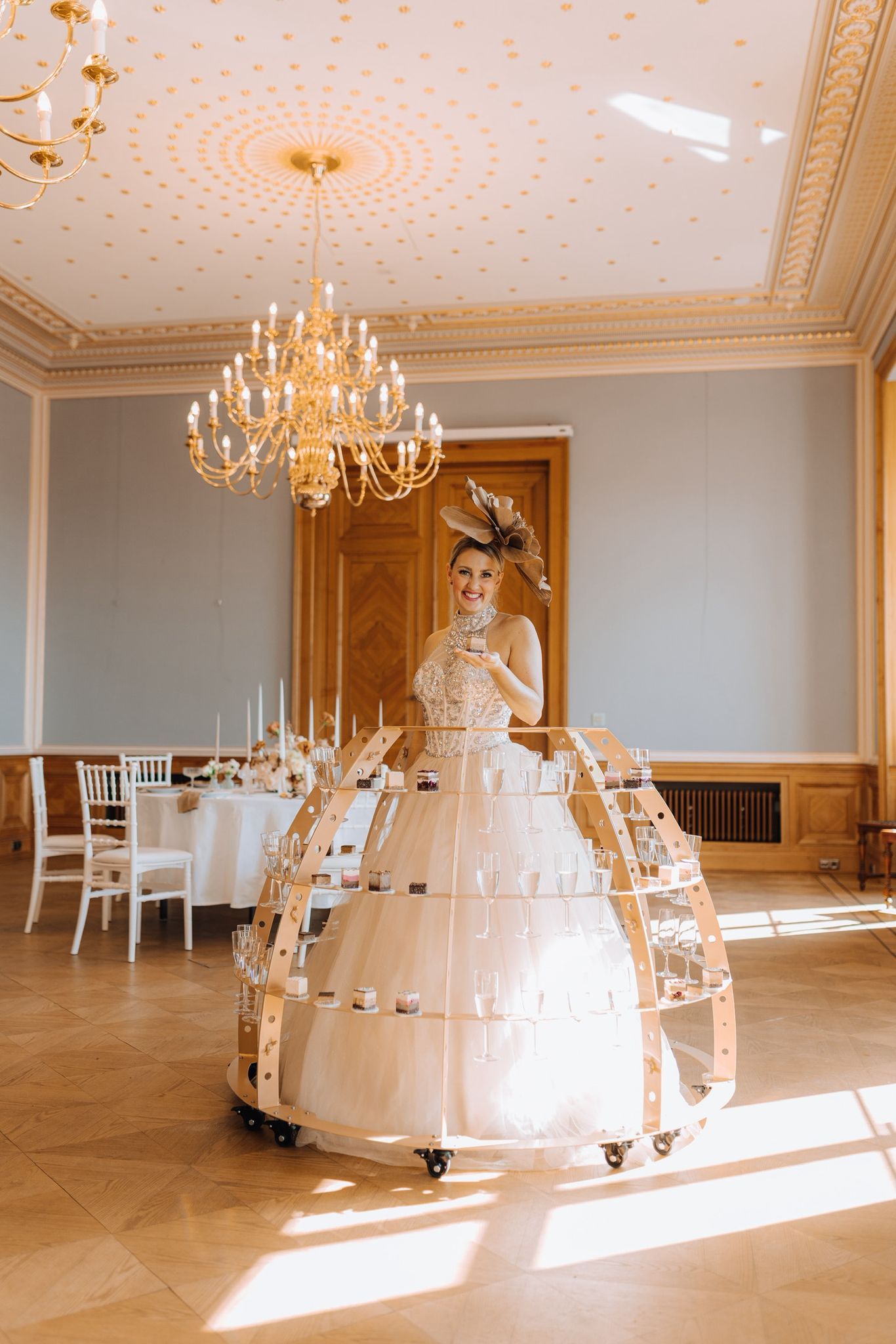 Elegant ballroom with herringbone floors, crystal chandeliers and sun streaming through windows creates a luxurious setting.