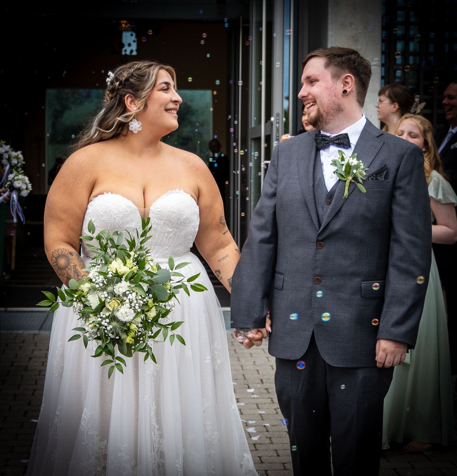Smiling bride and groom holding hands outside church surrounded by bubbles after ceremony.