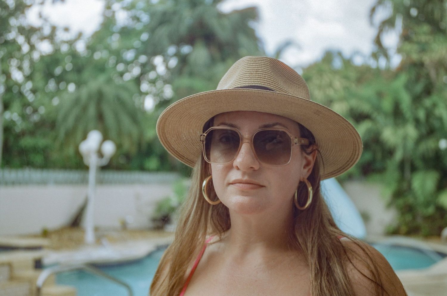 A relaxed poolside portrait featuring someone in a wide-brimmed hat and stylish sunglasses.
