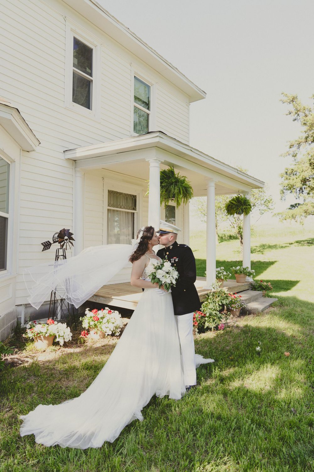 Wedding couple shares intimate moment outside white farmhouse with hanging plants.