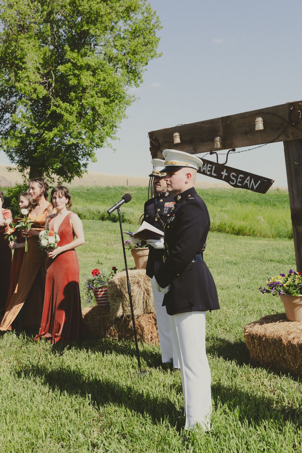 Outdoor wedding ceremony with military officiant standing near rustic wooden sign.