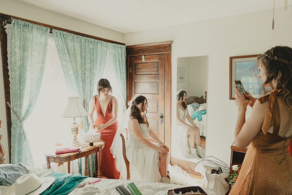 Getting ready scene in a sunlit bedroom with people in colorful dresses preparing for a special occasion.