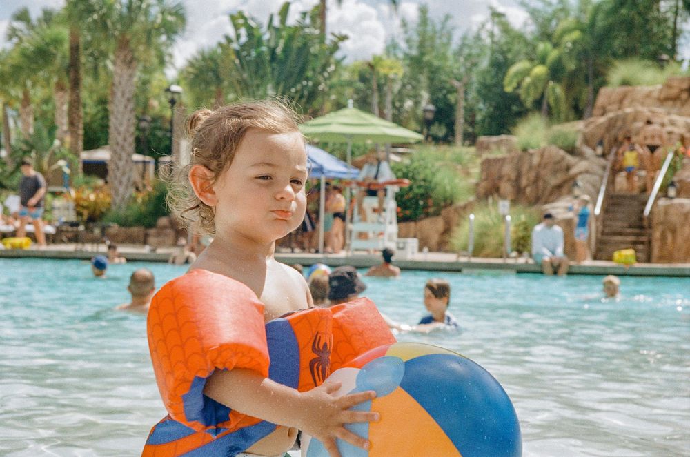 A child playing with colorful beach balls in a tropical resort pool with waterfalls.