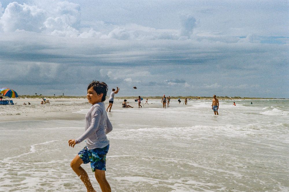 A joyful beach scene with people playing in the surf and sand on a cloudy summer day.