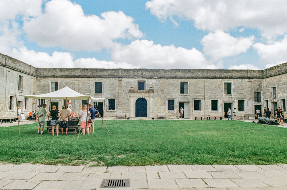 Stone courtyard of historic fort with green lawn and visitors exploring the grounds.