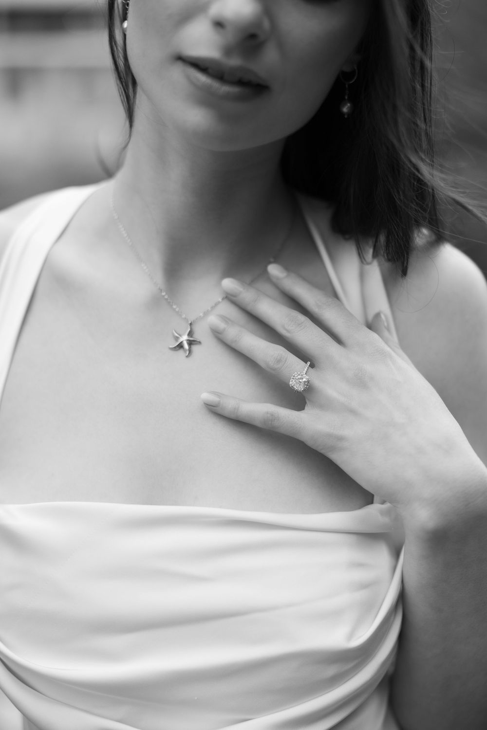 Black and white portrait showing elegant bride in white dress with draped neckline wearing delicate star pendant and ring.