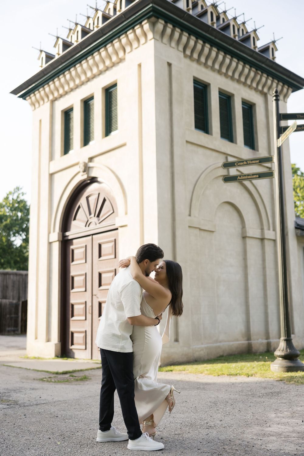 A romantic couple shares intimate moments in front of a white architectural structure with arched doorways.